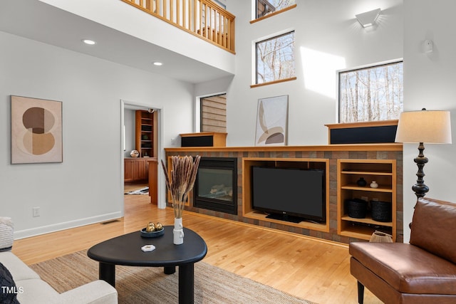 living room featuring wood finished floors, baseboards, a high ceiling, recessed lighting, and a glass covered fireplace