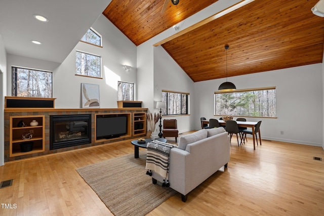 living room with visible vents, high vaulted ceiling, hardwood / wood-style flooring, a glass covered fireplace, and wood ceiling