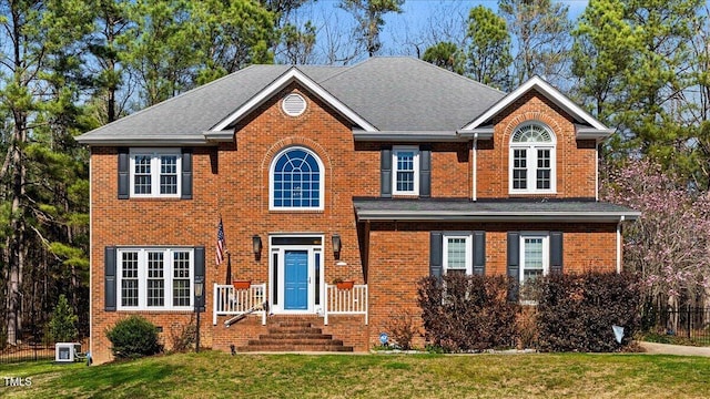 view of front of home with a front lawn, cooling unit, brick siding, and a shingled roof