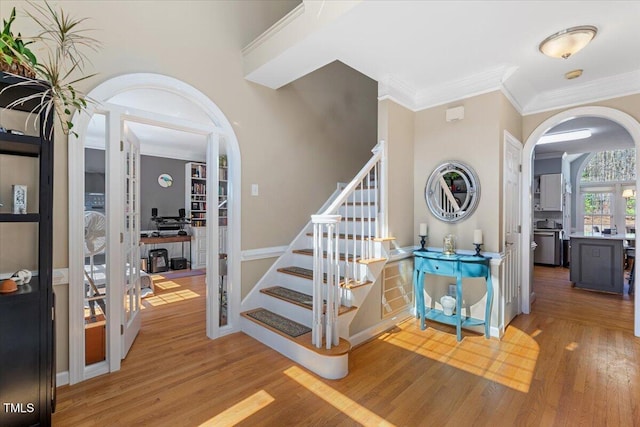 entrance foyer featuring stairway, arched walkways, wood finished floors, and crown molding