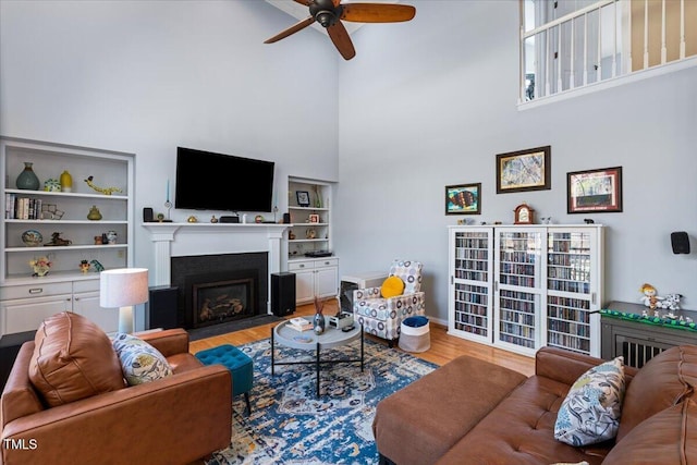 living area with wood finished floors, a fireplace with flush hearth, a ceiling fan, and built in features