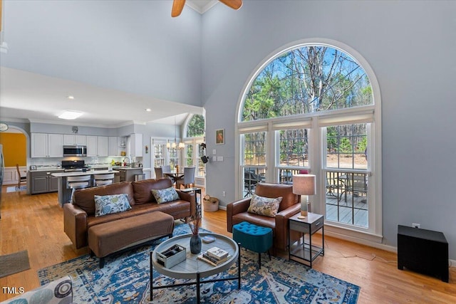 living area with light wood finished floors, ceiling fan with notable chandelier, and a high ceiling