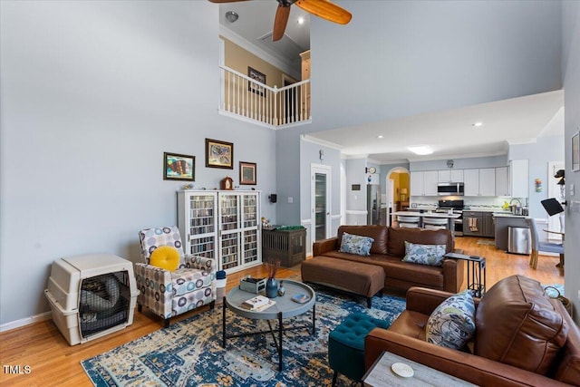 living room with a towering ceiling, ceiling fan, light wood-style floors, and ornamental molding