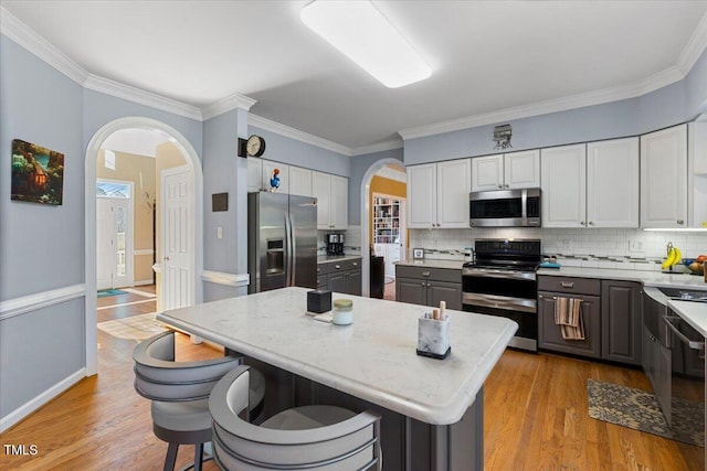 kitchen with arched walkways, appliances with stainless steel finishes, tasteful backsplash, and light wood-type flooring