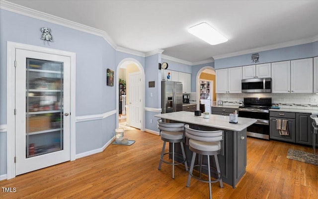 kitchen with light wood finished floors, arched walkways, appliances with stainless steel finishes, and light countertops