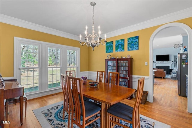 dining space featuring a notable chandelier, wainscoting, crown molding, and light wood-type flooring