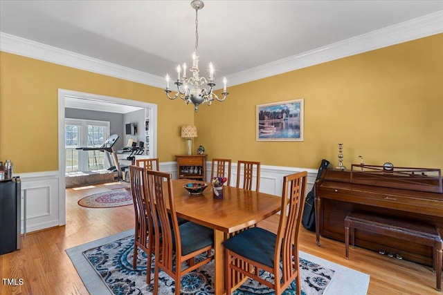 dining room with ornamental molding, wainscoting, light wood finished floors, and a chandelier