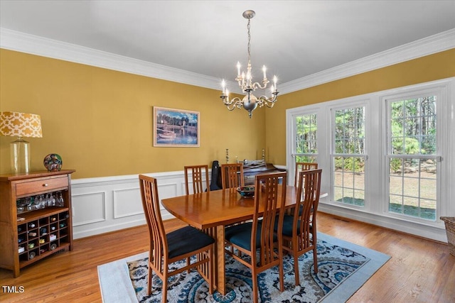 dining space featuring a notable chandelier, wood finished floors, a wainscoted wall, and ornamental molding