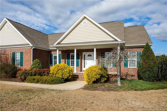 view of front facade with brick siding, covered porch, and roof with shingles