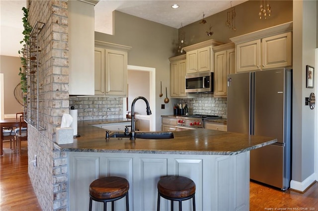 kitchen featuring a sink, dark countertops, cream cabinets, stainless steel appliances, and a peninsula