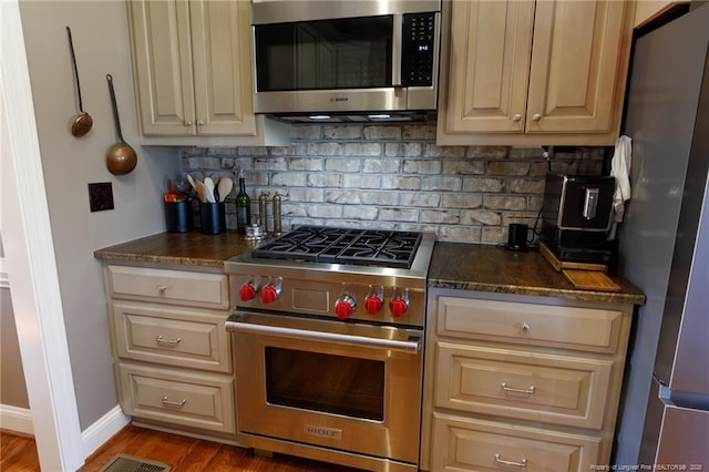 kitchen featuring wood finished floors, stainless steel appliances, dark stone counters, decorative backsplash, and baseboards