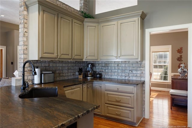 kitchen with dark stone countertops, backsplash, light wood-type flooring, and a sink