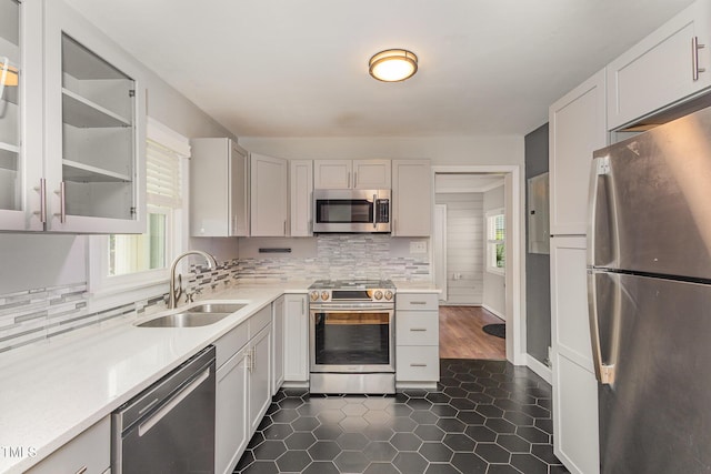 kitchen featuring a sink, light countertops, glass insert cabinets, appliances with stainless steel finishes, and backsplash