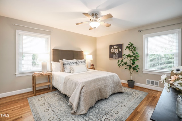 bedroom with ceiling fan, visible vents, baseboards, and wood finished floors