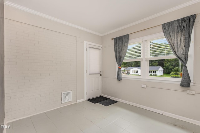 spare room featuring baseboards, ornamental molding, and brick wall