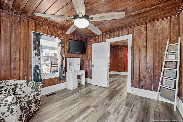 interior space with wooden walls, visible vents, wood ceiling, wood finished floors, and a ceiling fan