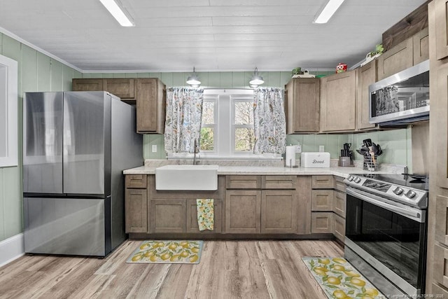 kitchen with a sink, stainless steel appliances, light wood-type flooring, and light countertops