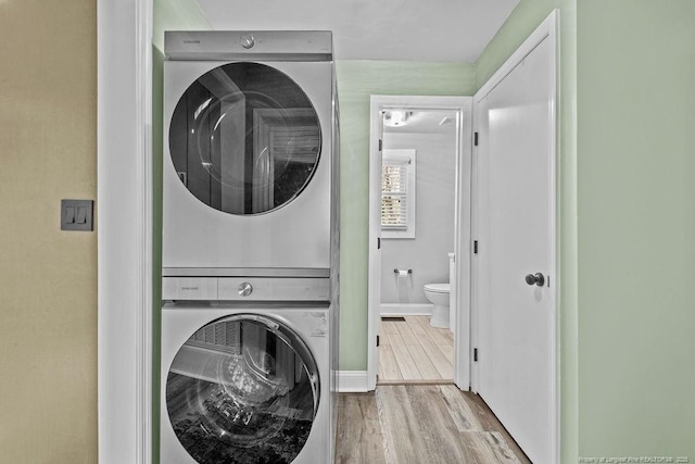 clothes washing area featuring baseboards, wood finished floors, laundry area, and stacked washing maching and dryer