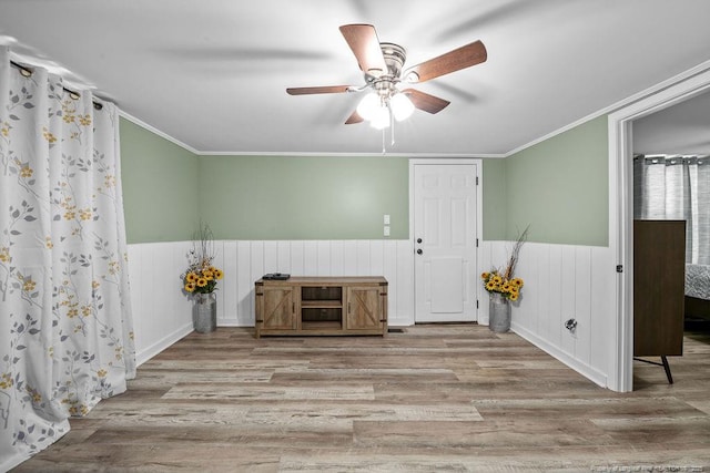 empty room with ceiling fan, wood finished floors, wainscoting, and ornamental molding