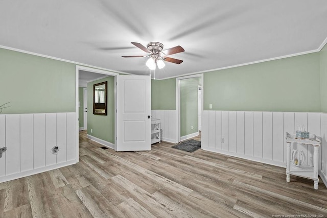 empty room with a wainscoted wall, ornamental molding, ceiling fan, and wood finished floors