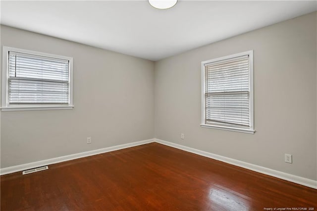 empty room featuring visible vents, a healthy amount of sunlight, and wood finished floors