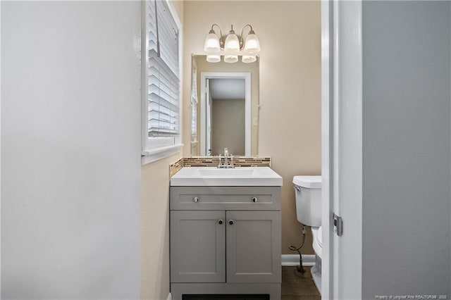 half bathroom featuring a chandelier, backsplash, vanity, and toilet