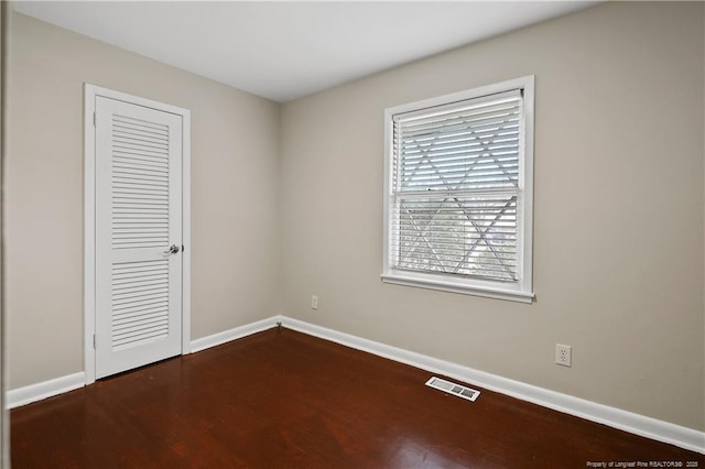 unfurnished bedroom featuring dark wood finished floors, visible vents, a closet, and baseboards