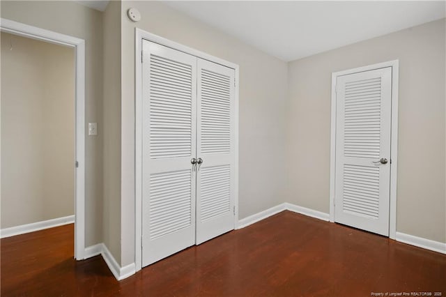 unfurnished bedroom with a closet, dark wood-type flooring, and baseboards