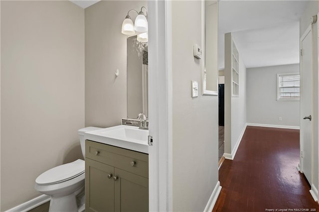 bathroom with toilet, vanity, baseboards, and wood finished floors