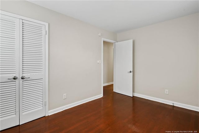 unfurnished bedroom featuring wood finished floors, baseboards, and a closet