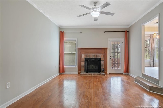 unfurnished living room featuring a brick fireplace, baseboards, ornamental molding, a ceiling fan, and wood-type flooring