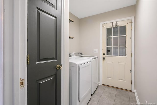 clothes washing area with laundry area, light tile patterned flooring, washing machine and dryer, and baseboards