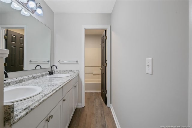 bathroom with a sink, baseboards, wood finished floors, and double vanity