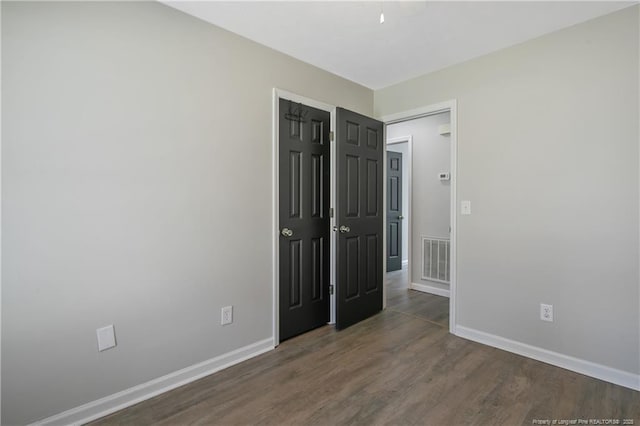 unfurnished bedroom featuring visible vents, baseboards, and dark wood-style flooring