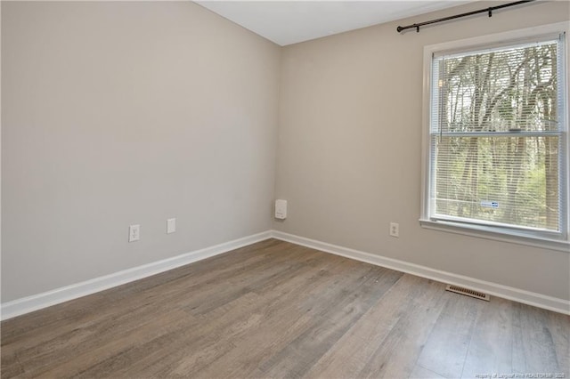 spare room featuring wood finished floors, a healthy amount of sunlight, visible vents, and baseboards