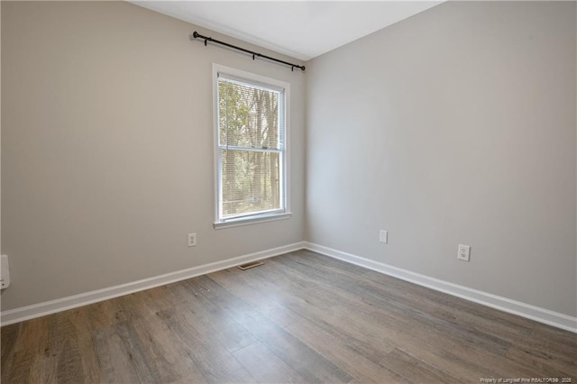 empty room with dark wood finished floors, visible vents, and baseboards