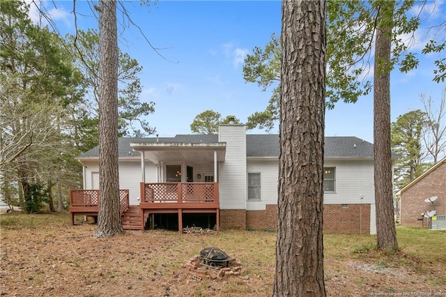 back of property featuring a wooden deck, a fire pit, a chimney, and a shingled roof