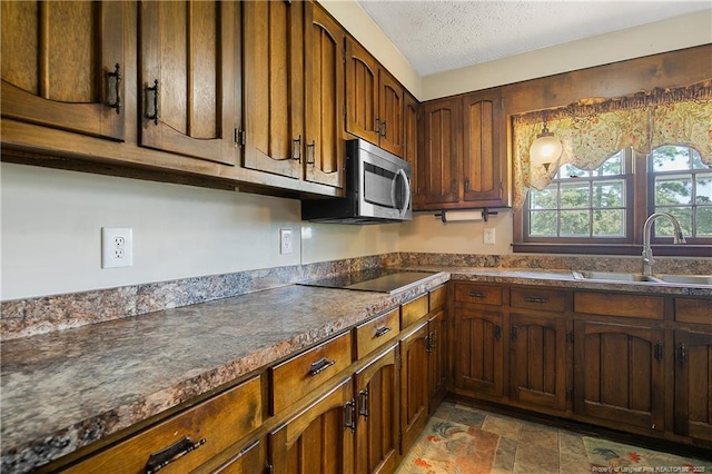 kitchen featuring a sink, stainless steel microwave, dark countertops, and black electric cooktop