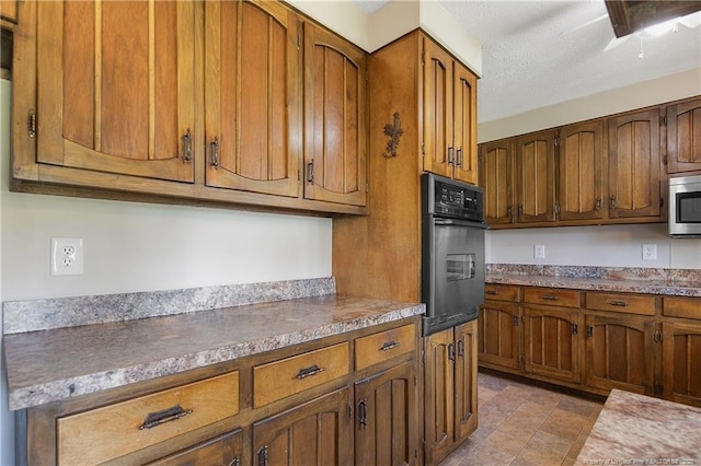 kitchen with stainless steel microwave, black oven, brown cabinets, and a textured ceiling