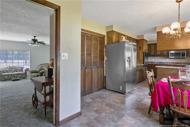 kitchen featuring a textured ceiling, ceiling fan with notable chandelier, dark colored carpet, and stainless steel appliances