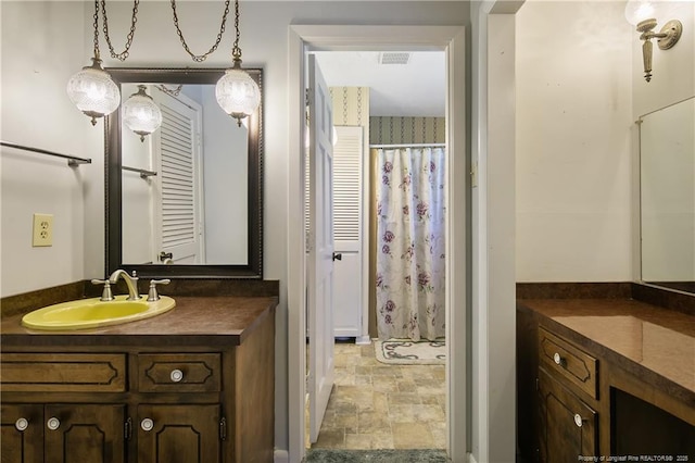 bathroom with visible vents, curtained shower, vanity, and stone finish flooring