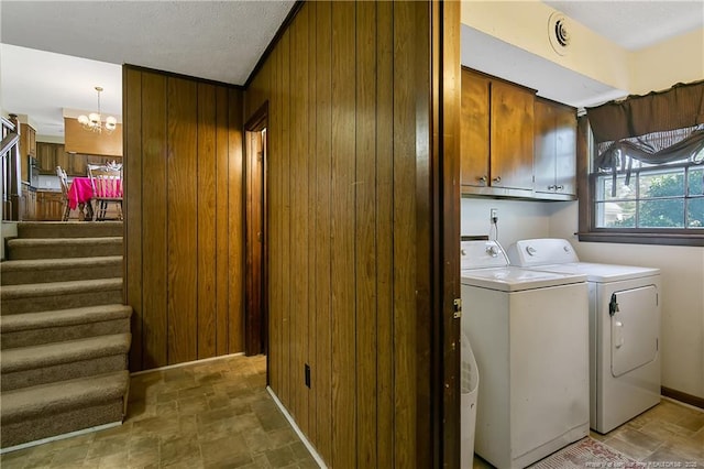 washroom featuring a notable chandelier, stone finish floor, washer and clothes dryer, cabinet space, and wood walls