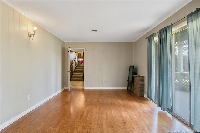 empty room with stairs, light wood-type flooring, baseboards, and ornamental molding