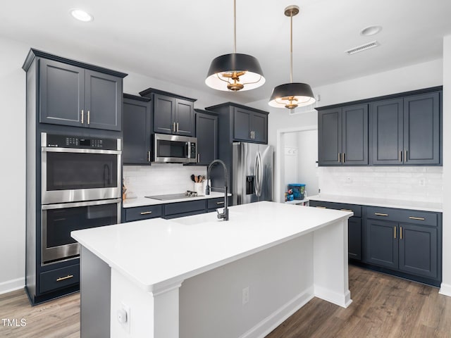 kitchen with visible vents, light countertops, appliances with stainless steel finishes, wood finished floors, and a kitchen island with sink