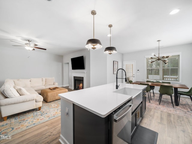 kitchen with a sink, open floor plan, a lit fireplace, light wood-style flooring, and stainless steel dishwasher