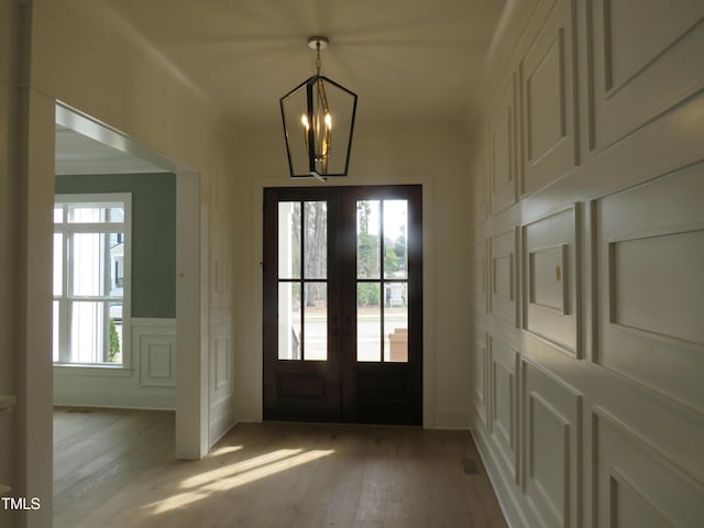 entryway featuring french doors, light wood finished floors, a notable chandelier, and a decorative wall