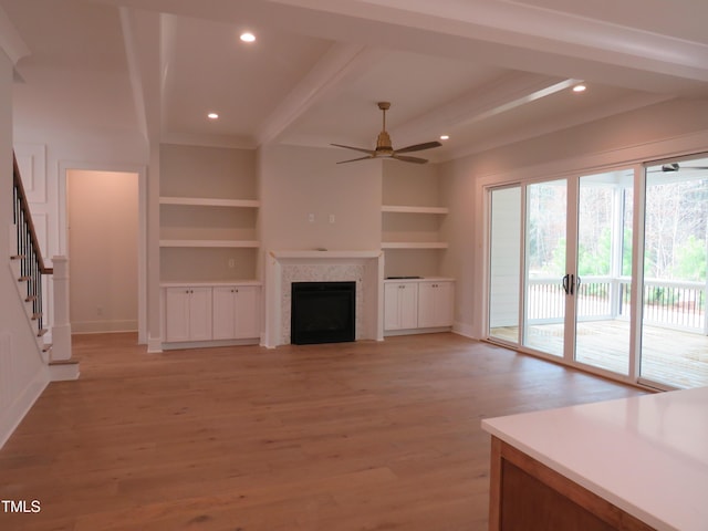 unfurnished living room featuring light wood-type flooring, beamed ceiling, a fireplace, ceiling fan, and stairs