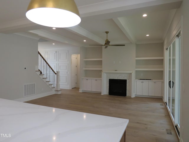 unfurnished living room with beamed ceiling, visible vents, a ceiling fan, light wood finished floors, and stairs