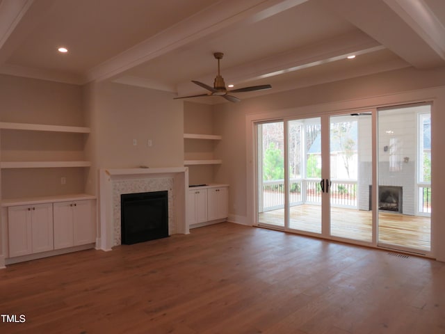 unfurnished living room with beamed ceiling, built in shelves, wood finished floors, a fireplace, and ceiling fan