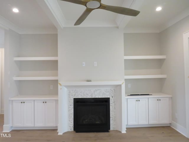 unfurnished living room with crown molding, built in features, a ceiling fan, and light wood finished floors